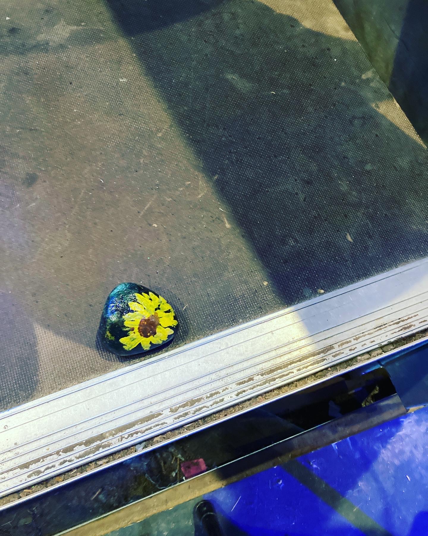 A handpainted rock, featuring a bright yellow sunflower with a dotted black and brown centre, is tucked into a corner in front of a row of seats at Bard on the Beach.