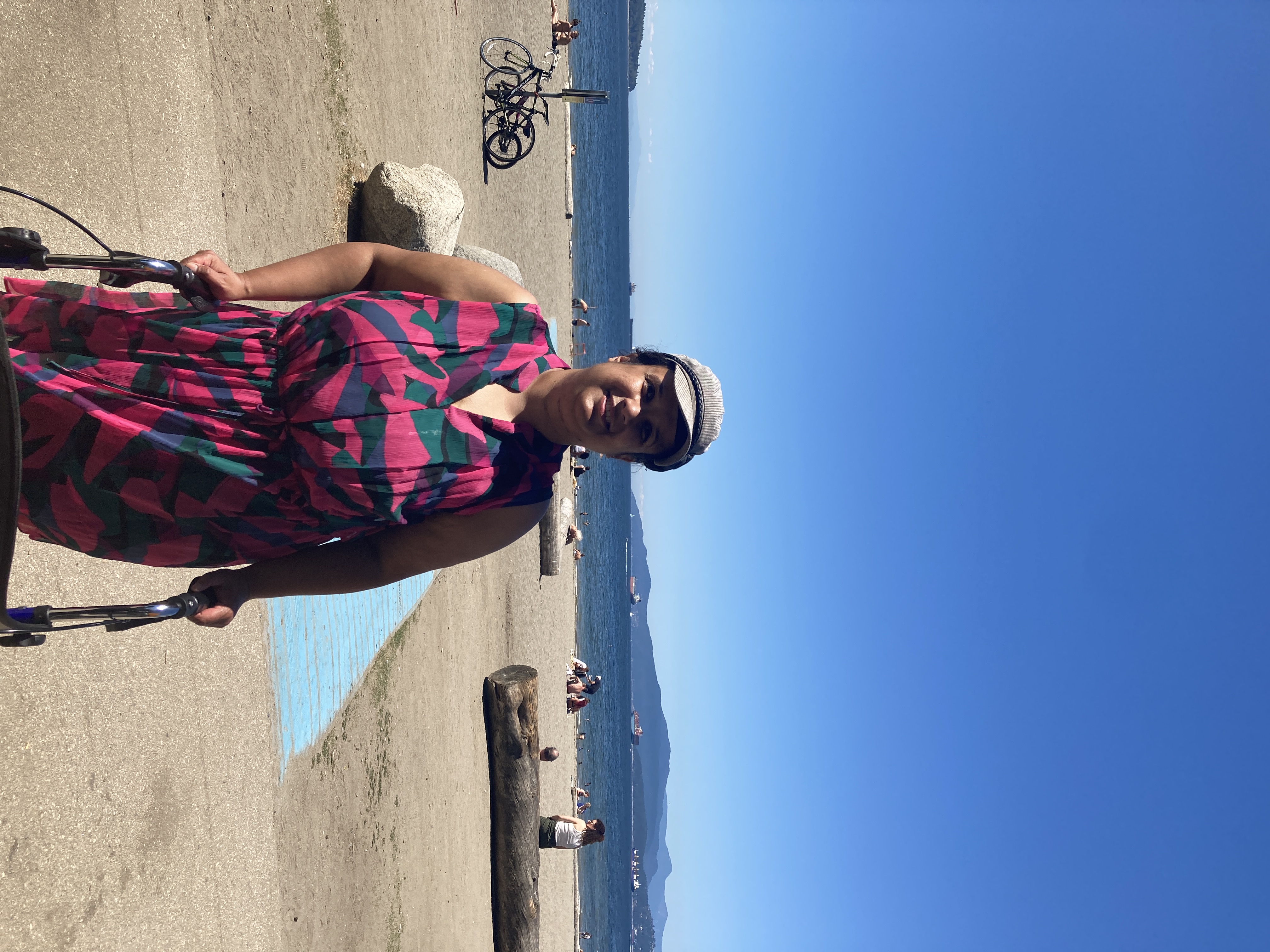 Kristy stands supported by her walker with the ocean and sand of English Bay, Vancouver behind her