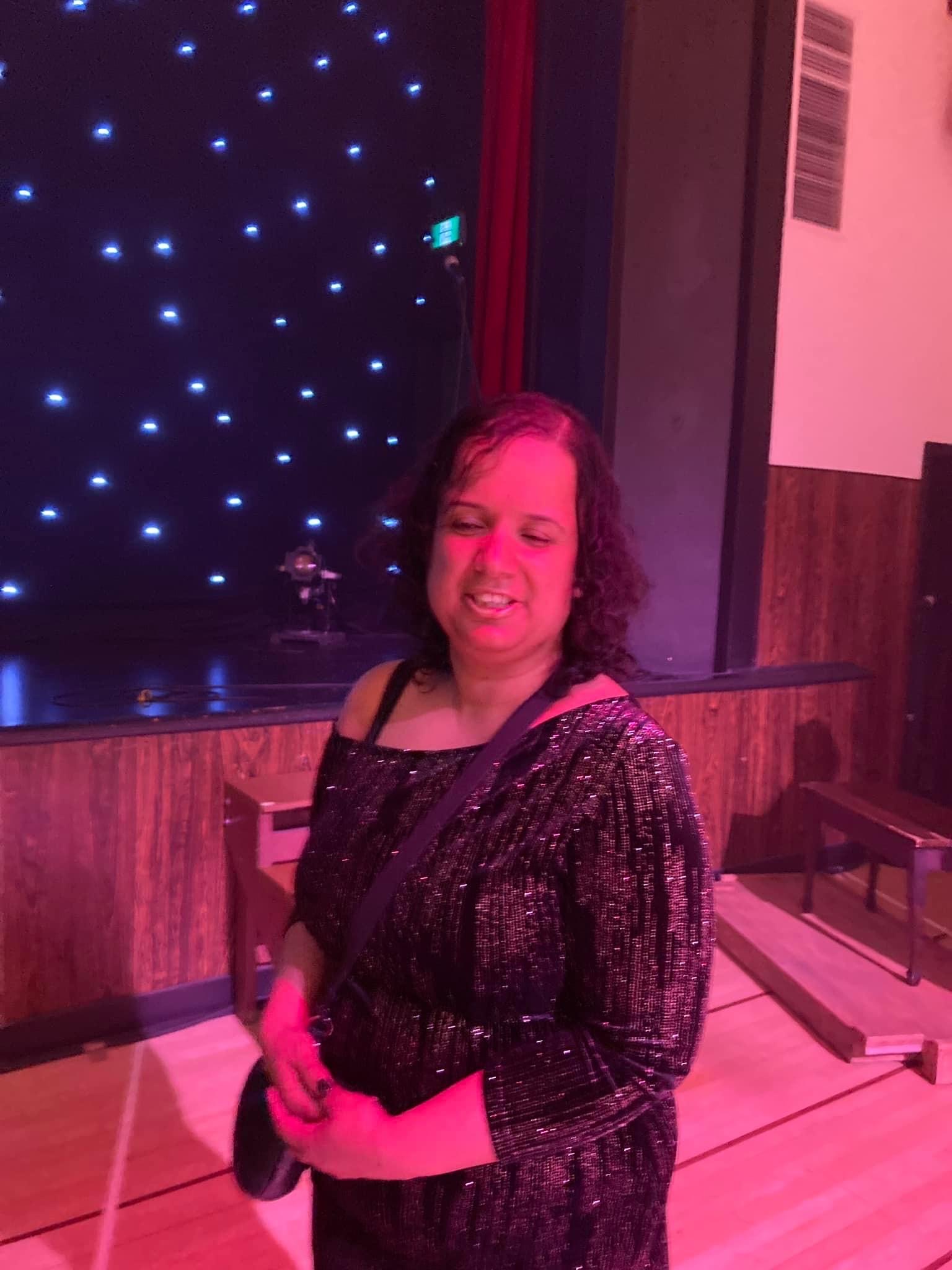 Kristy after the debut performance, wearing a rose-gold and black velvet tunic and posing with fairy lights in the background.