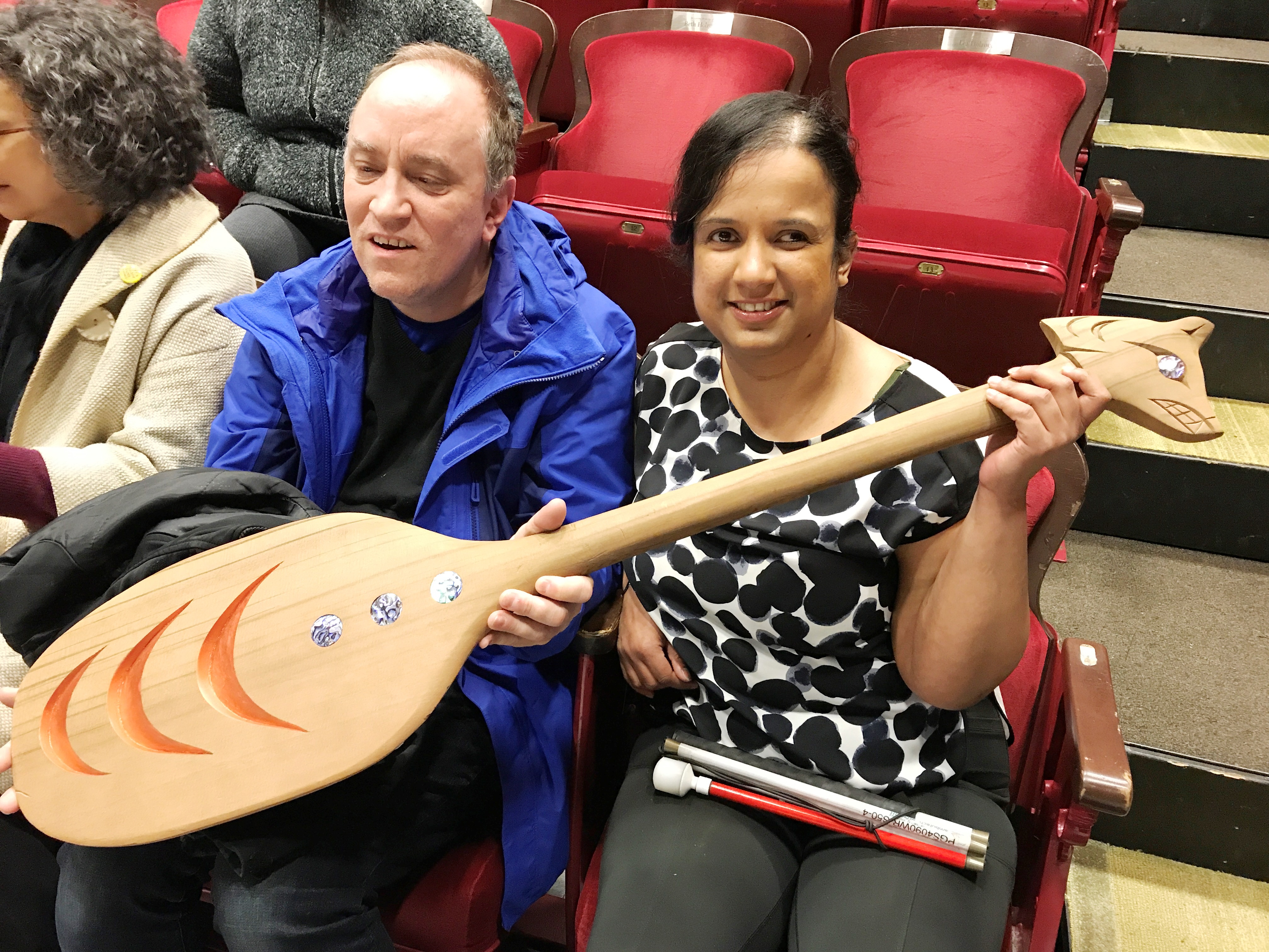 Shawn and Kristy during the Skyborn touch tour holding a paddle, decorated with abalone and carved with a wolf's head.