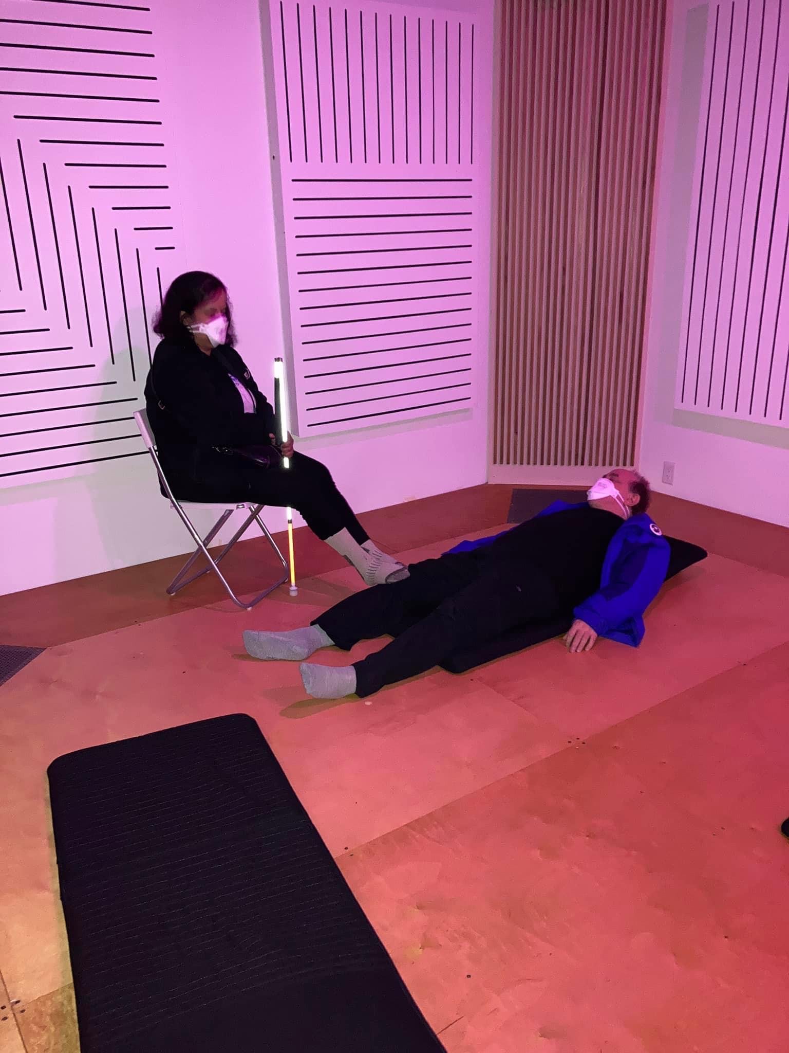 Kristy sits in a folding chair against a wall while Shawn lies on a foam mat at Lobe Studios in Vancouver.